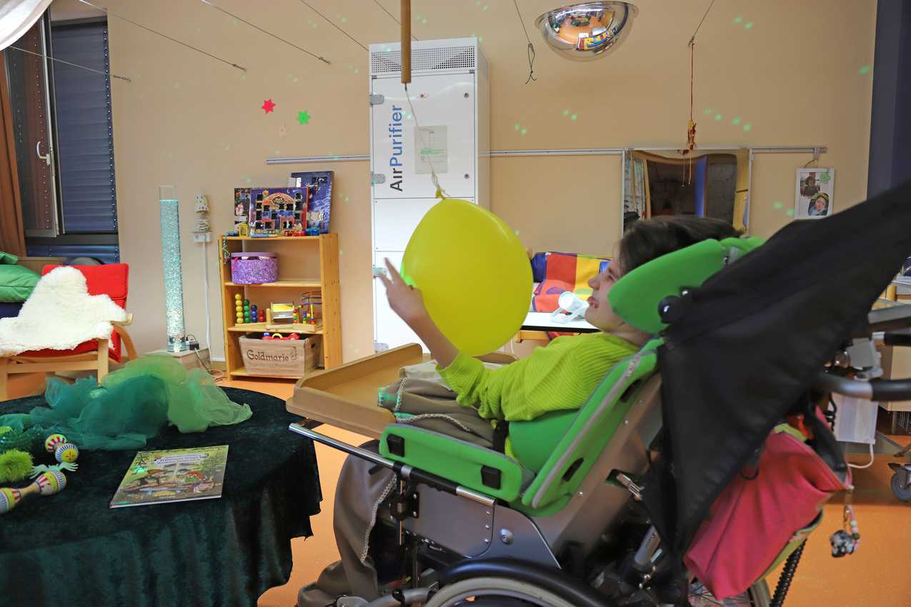 In einem Ruheraum der Schule Wittekindshof steht ein Luftreiniger, während ein Mädchen in einem Rollstuhl mit einem Ballon spielt.